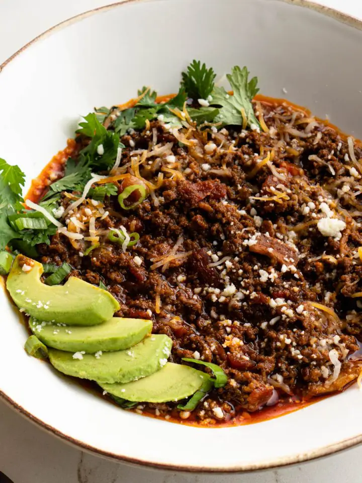 Bowl of chili garnished with avocado, cheese, and cilantro