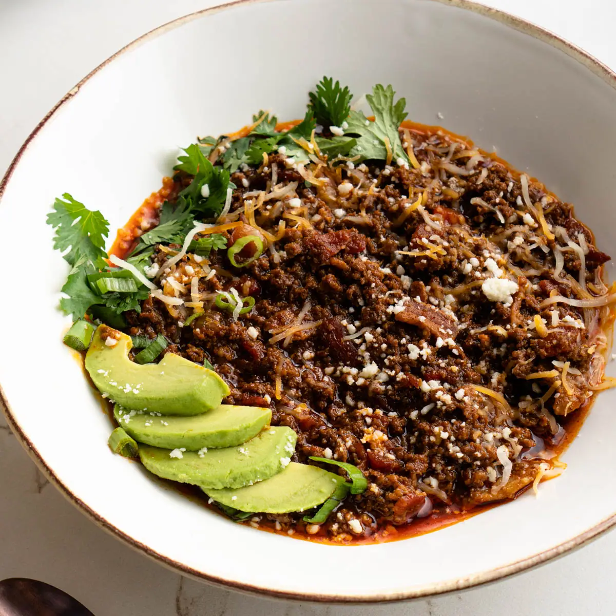 Bowl of chili garnished with avocado, cheese, and cilantro
