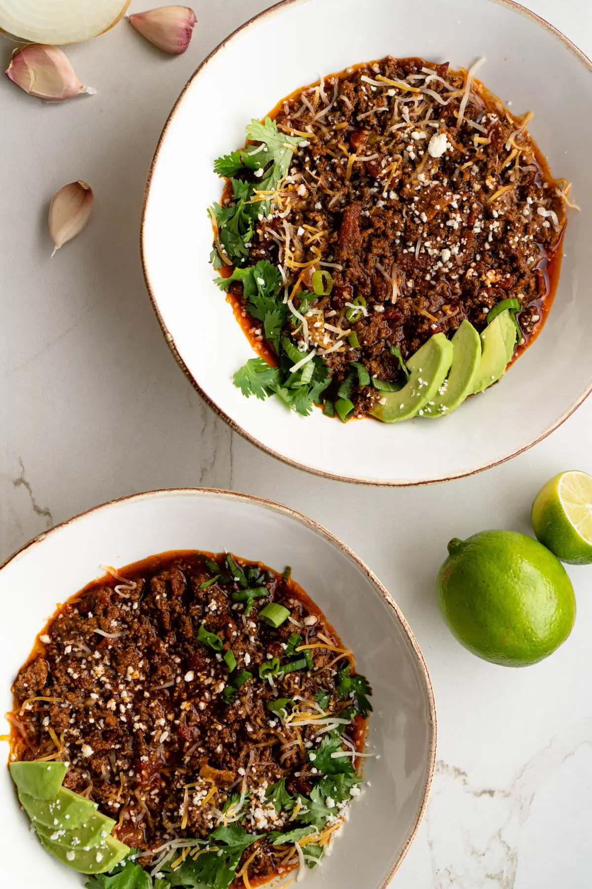 Two bowls of chili near garlic cloves and lime