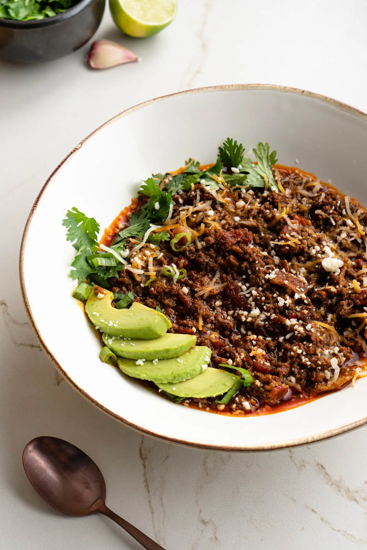 Keto chili con carne with avocado slices, cilantro, green onion, and cheese toppings.