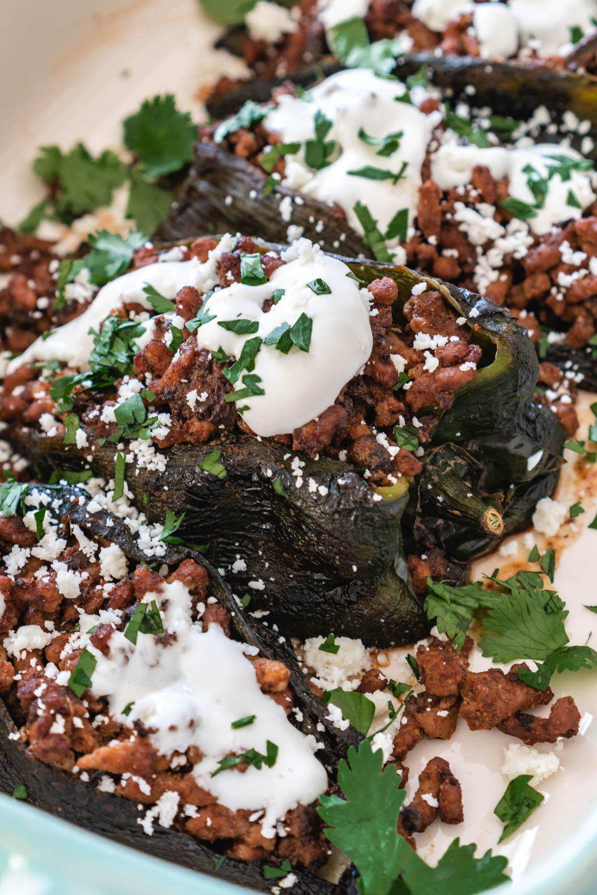 Stuffed poblano peppers in casserole dish topped with cilantro and Mexican crema.