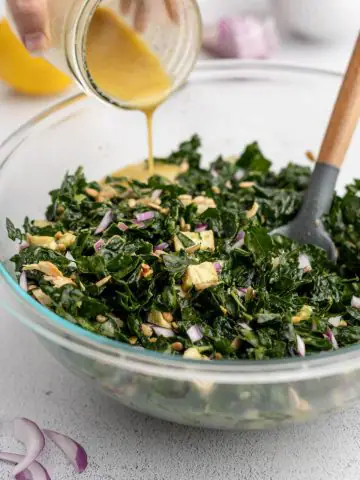 Lemon dressing poured into kale salad with avocado, chicken, and red onion.