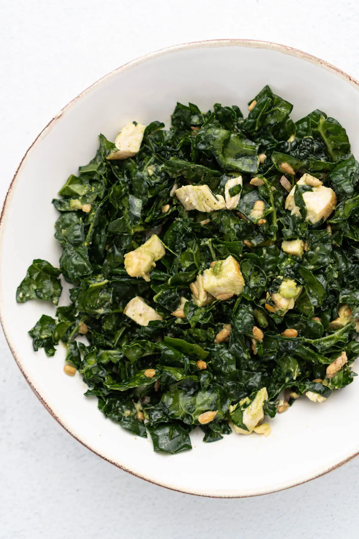 Chicken and kale salad in shallow white bowl.