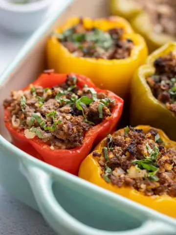 Baked stuffed red, yellow, and green peppers in blue casserole dish.