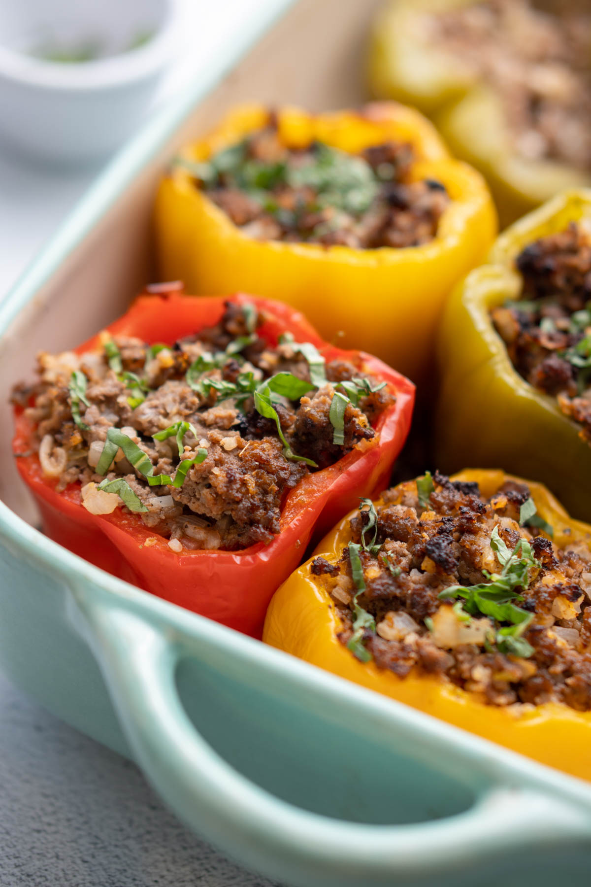 Bell peppers stuffed with ground beef mixture in casserole dish garnished with fresh basil.