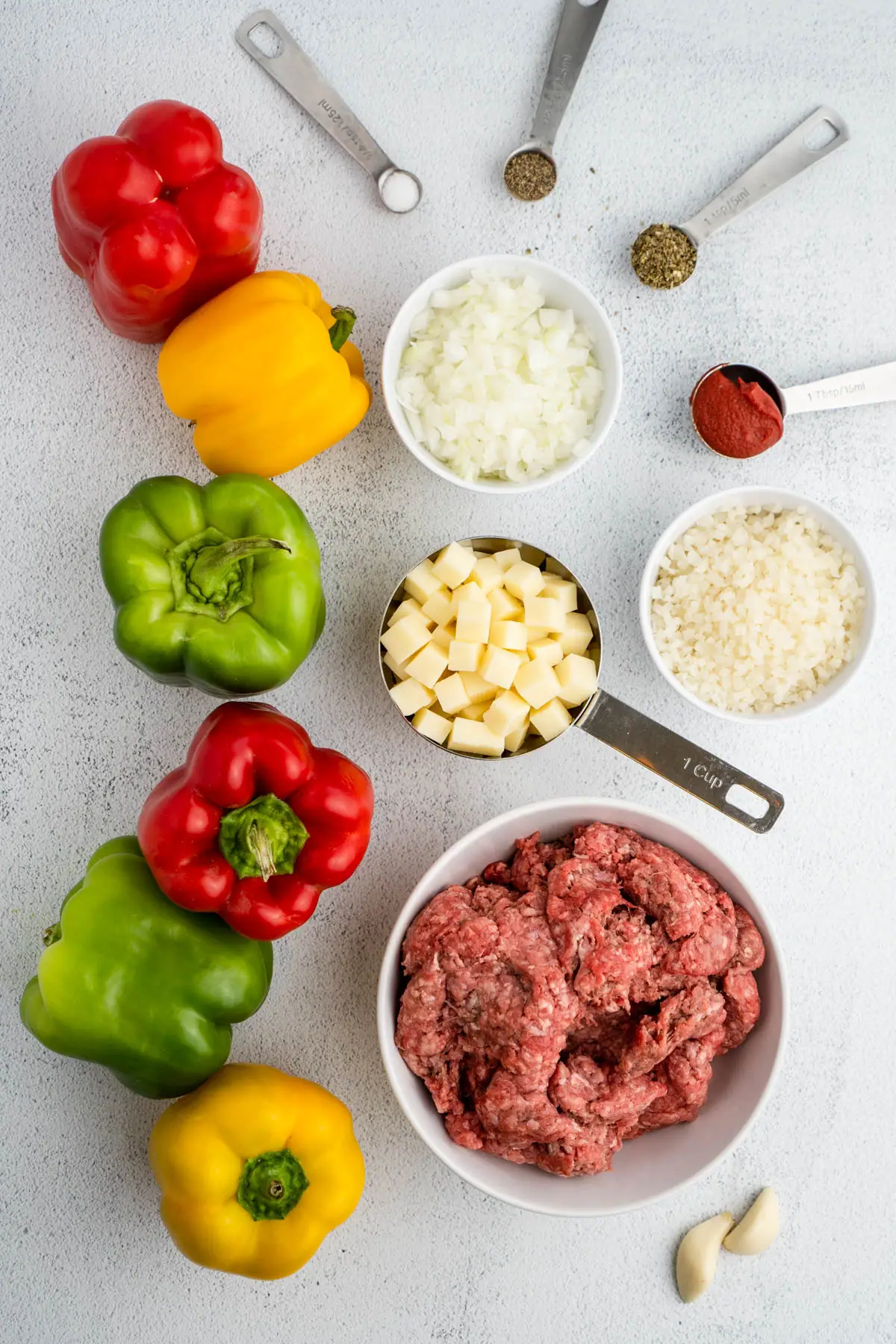Ingredients to make the recipe, including green, red, and yellow bell peppers, salt, pepper, Italian seasoning, tomato paste, riced cauliflower, onions, mozzarella cheese, ground beef, and garlic.